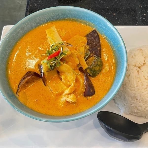A blue bowl of Urban Thai Kitchen's red curry with chicken, vegetables, and a side of white rice.