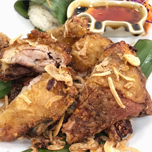 Crispy fried chicken pieces with fried garlic, sticky rice, and dipping sauce on a banana leaf.
