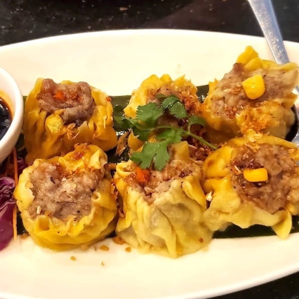 Six Thai dumplings with meat filling, garnished with cilantro and corn, served with dipping sauce.
