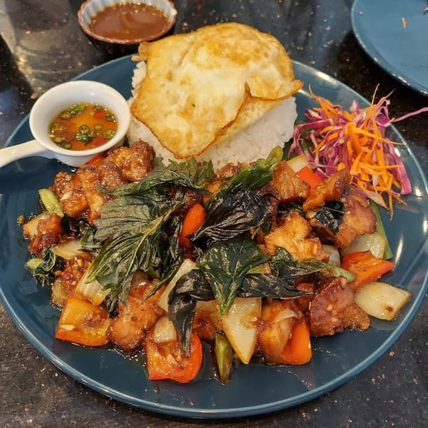A Thai basil chicken dish with rice, a fried egg, and shredded vegetables on a blue plate.