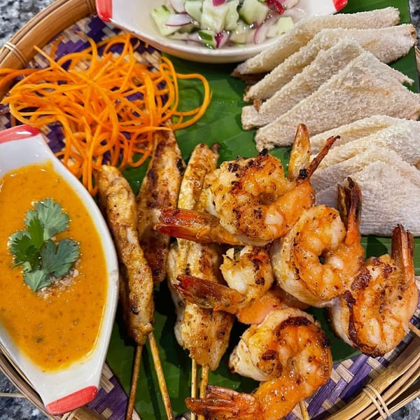 Thai platter with grilled shrimp and chicken skewers, peanut sauce, cucumber salad, and white bread triangles.